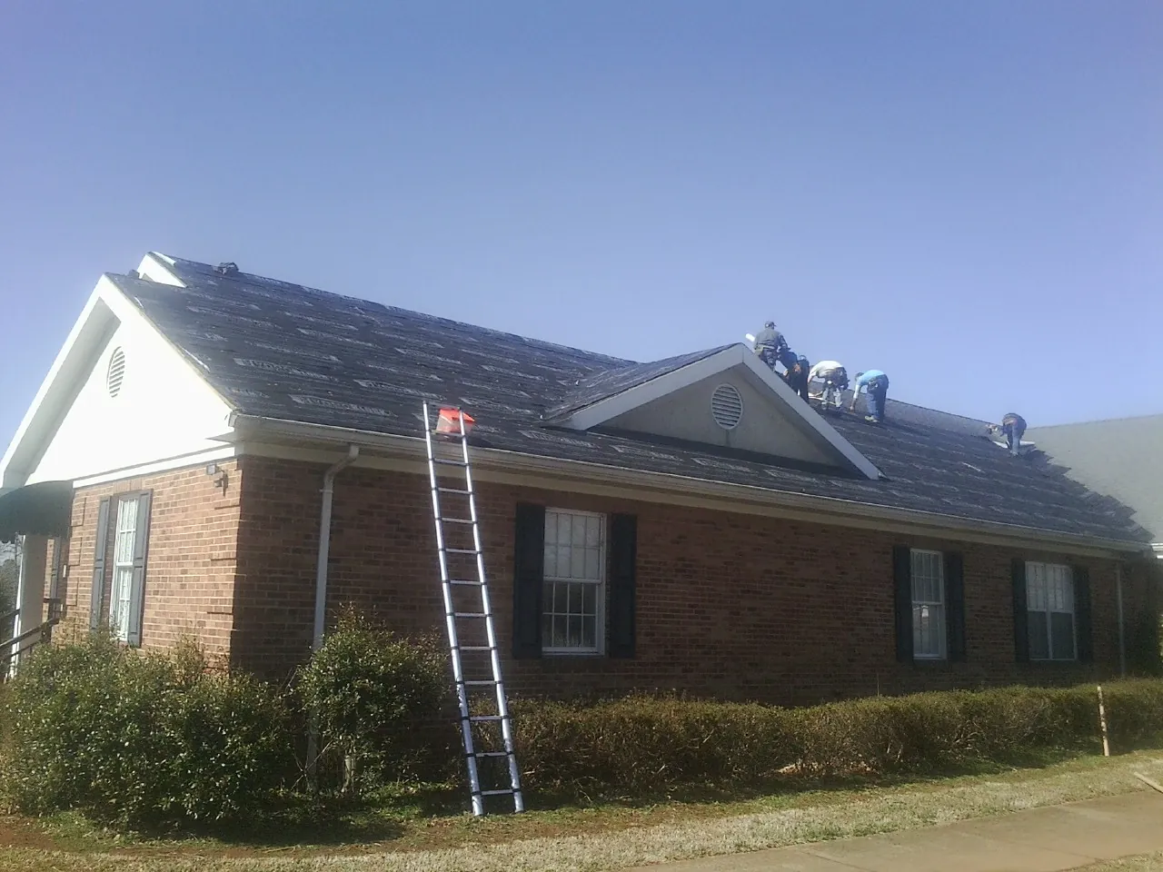 Crew tearing shingles off a brick ranch roof with a ladder set — Metal Roof Repair work by our crew in Goose Creek