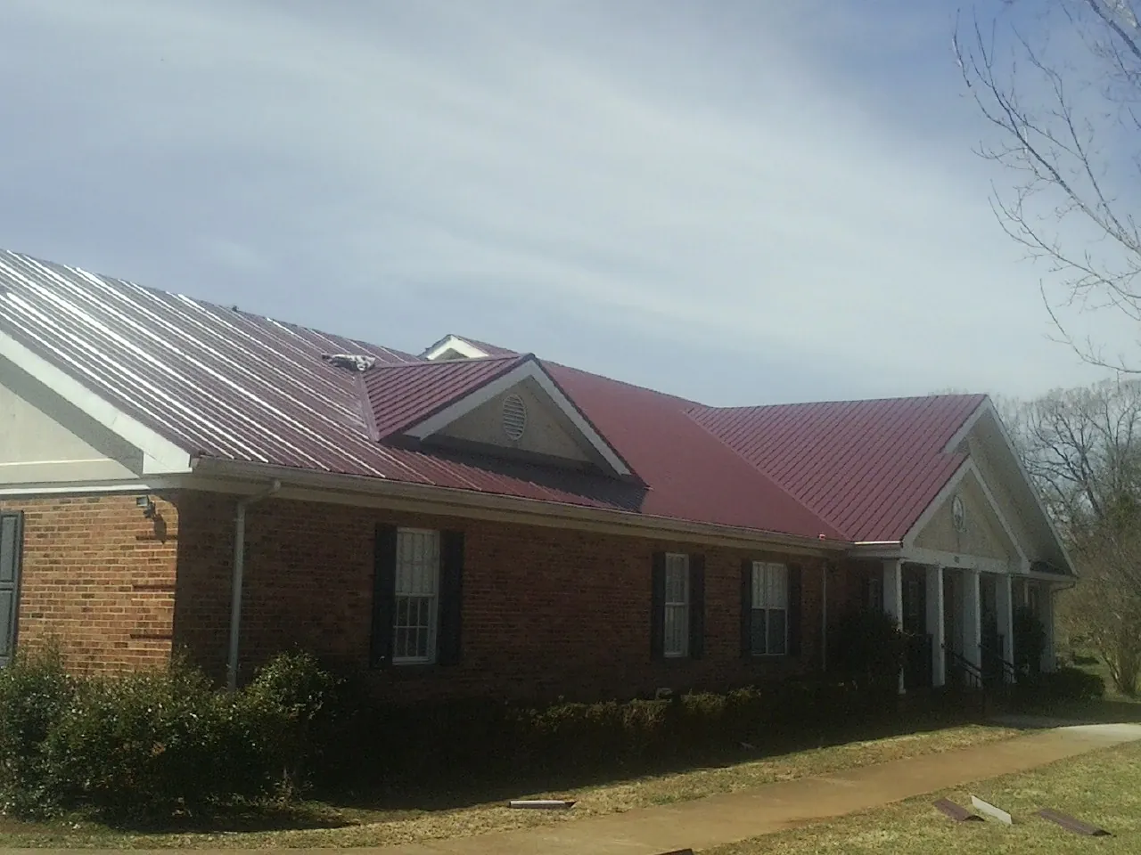 Red metal roof with gabled entries on a long brick building, from a Hail Damage Roof Repair job in Goose Creek