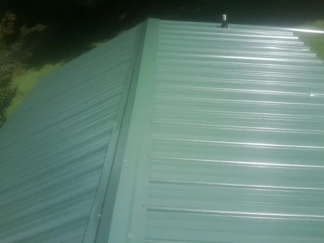 New green metal panels meeting at the ridge of a roof — Flat Roof Repair work by our crew in Goose Creek