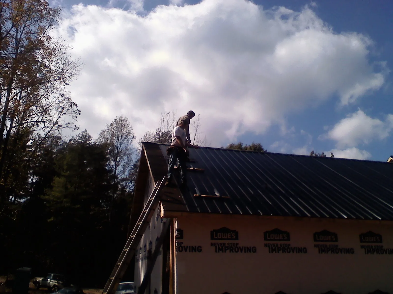 Roofer fastening dark metal panels high against a cloudy sky, from a Roof Inspection job in Goose Creek