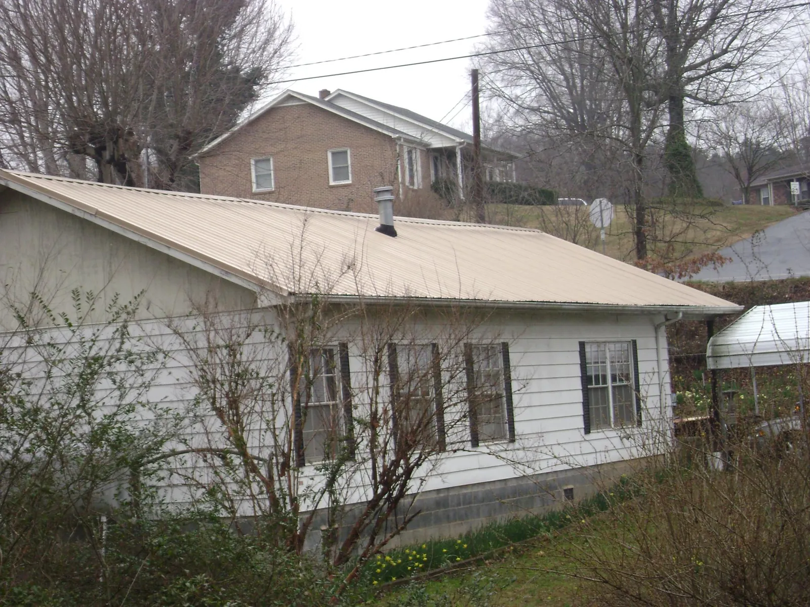 Tan metal roof on a white sided house set into a hillside — Commercial Roofing by Roofing Brothers in Goose Creek