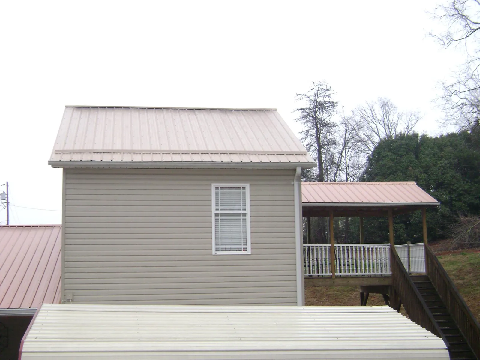 Tan metal roofs on a two story addition and attached porch, from a Roof Replacement job in Goose Creek